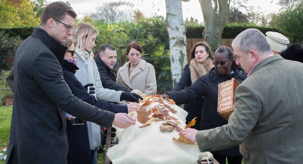 A burial shroud surrounded by people and covered with leaves.
