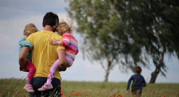 A father carrying two of his children in a field of poppies while his son runs ahead