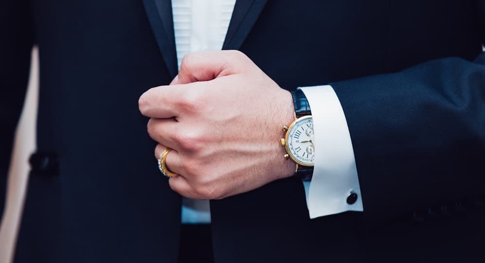 Man wearing a black suit with focus on his hand and watch.