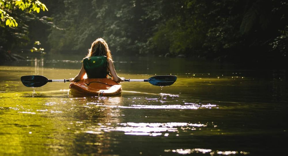 A woman in a kayak on a sunlit woodland river