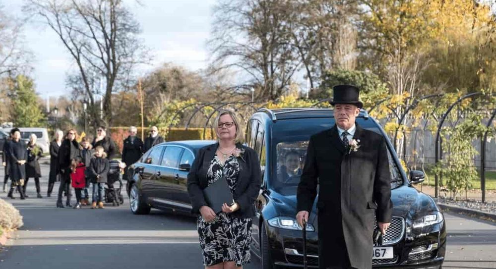 Funeral directors walk at the front of a funeral cortege.