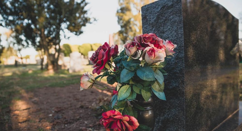 memorial vase with roses inside next to a headstone