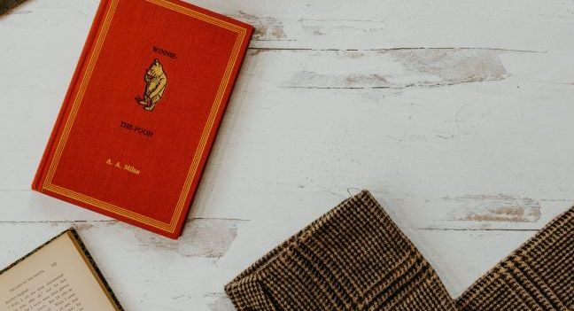 Red Winnie the Pooh book on a wooden table with a satchel and blazer