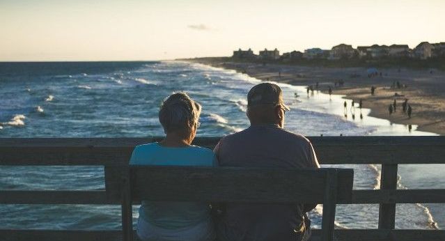 An old couple sit on a bench looking at the sea as the sun sets
