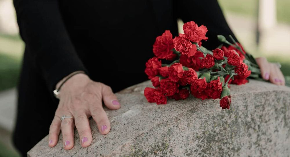 A woman wearing black places flowers on the grave of a loved one