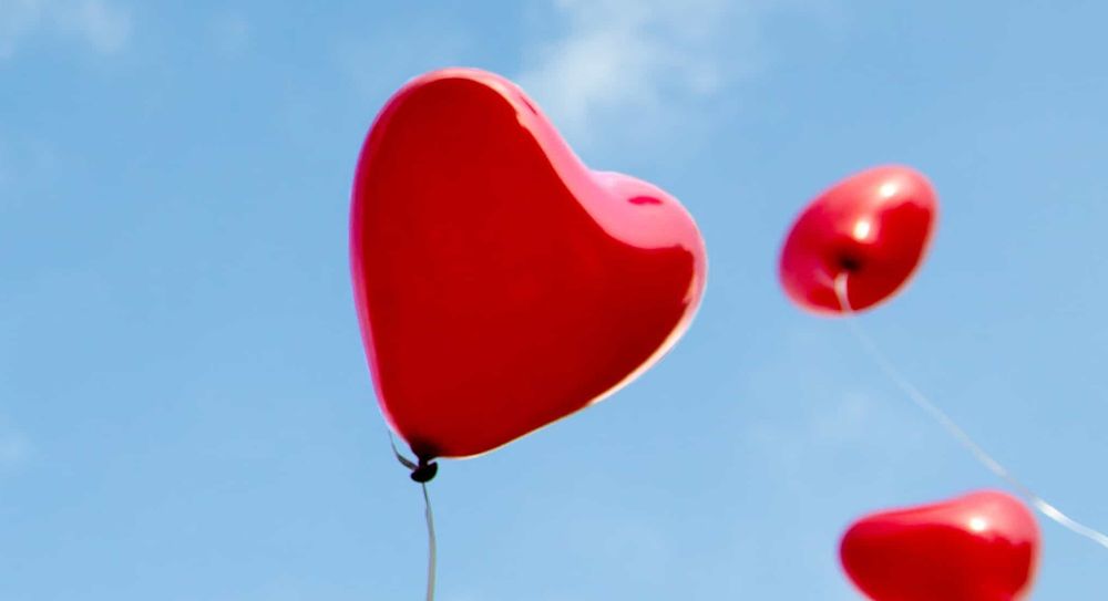 Red heart shaped balloons released into the sky.