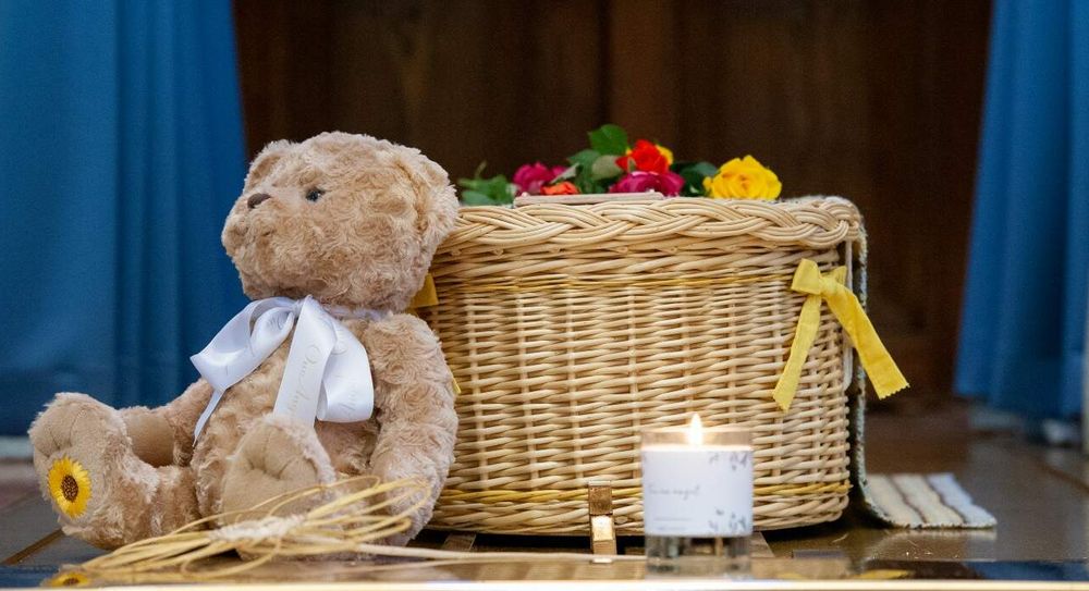 A child's coffin with teddy bear and candle.