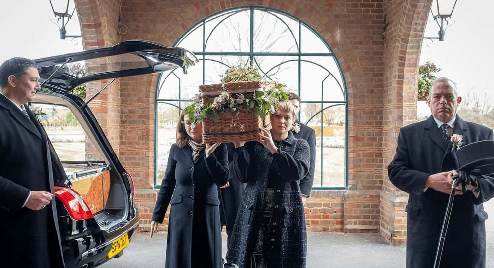 Funeral directors and mourners carry a coffin