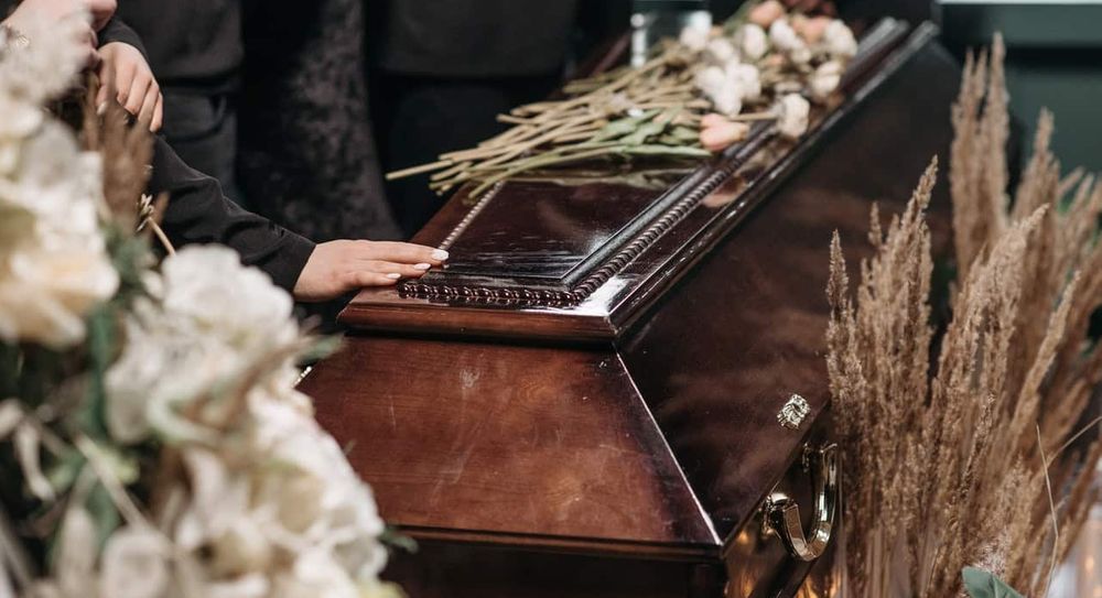 Person dressed in black with their hand on coffin.