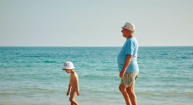 A grandad and grandson walk along the beach together