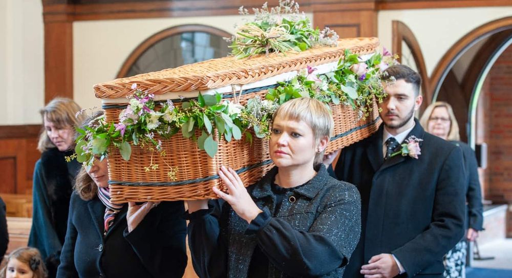 Pallbearers carrying a wicker coffin on their shoulders.