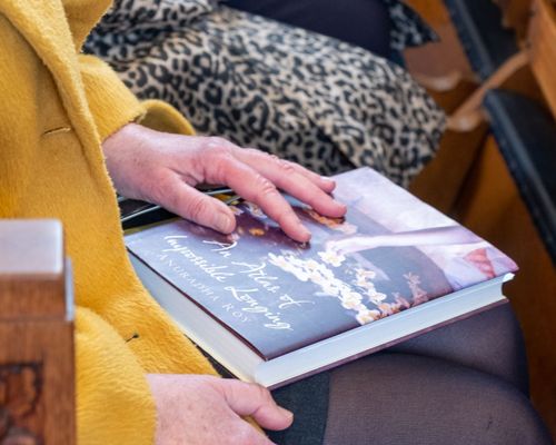 Close up of a woman sat on a church pew with a book on her lap