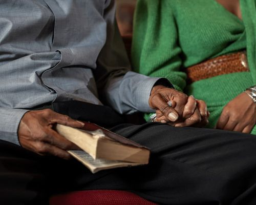 A couple holding hands at church. One of them holds a bible ready for a reading