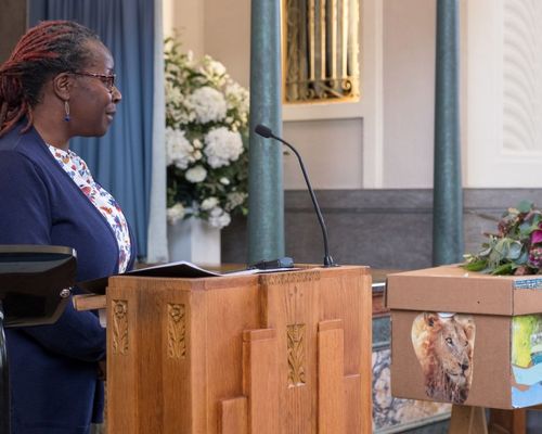 Woman speaking at a podium at a funeral with flowers