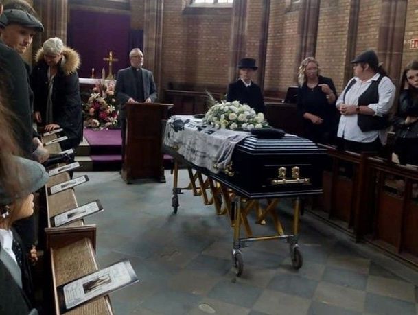 funeral service in church with coffin and orders of service resting on benches