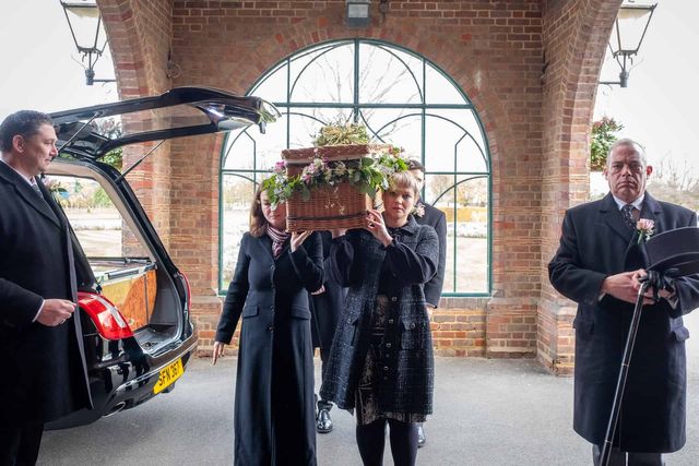 Funeral director and mourners carrying a coffin.