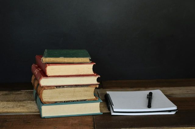 Pile of books and a writing pad on a wooden desk