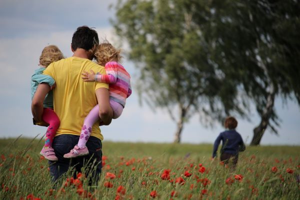 A father carrying two of his children in a field of poppies while his son runs ahead
