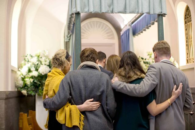 Guests at a funeral service with their arms around one another.