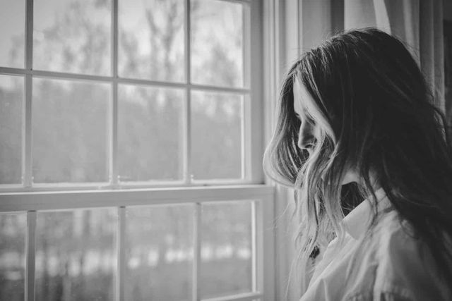 A black and white image of a woman looking out of the window.