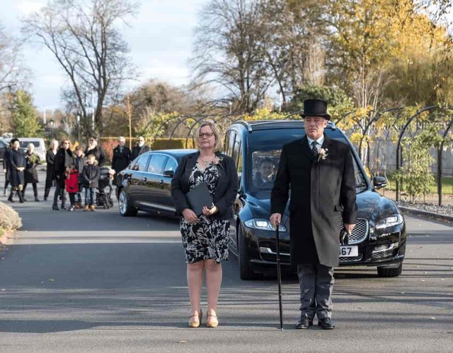 Funeral directors walk at the front of a funeral cortege.