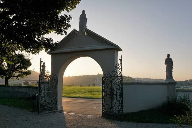 Open cemetery gateway at sunset with statues in silhouette 