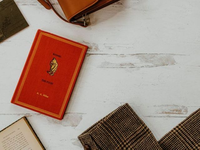 Red Winnie the Pooh book on a wooden table with a satchel and blazer