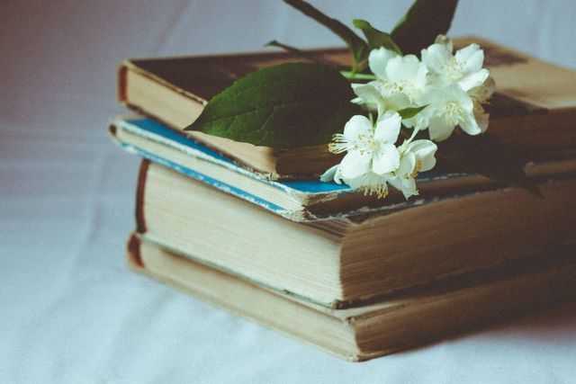 A pile of old books with some flowers on top.