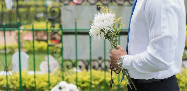 Man standing at a graveside at a funeral holding flowers. 