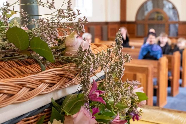 wicker coffin covered in flowers in a church