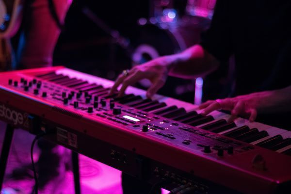 A musician plays an electric keyboard under neon pink lighting