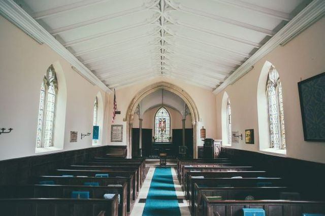 Central aisle of a chapel with pews on either side and a stained glass window at the far end