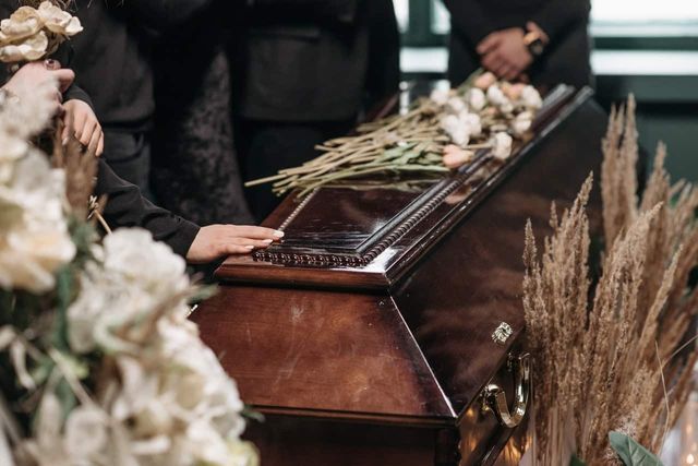 Person dressed in black with their hand on coffin.