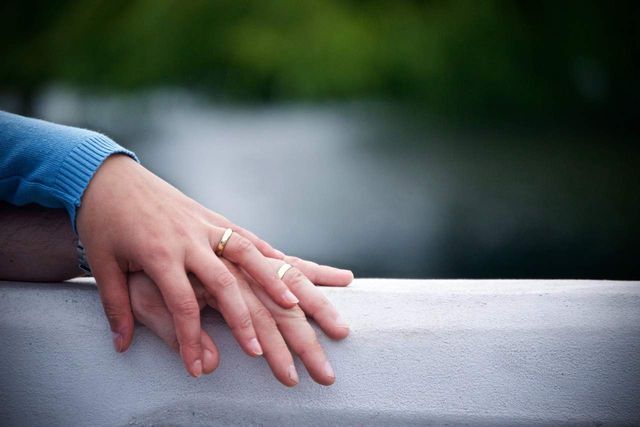 Two hands wearing wedding rings resting on top of one another.