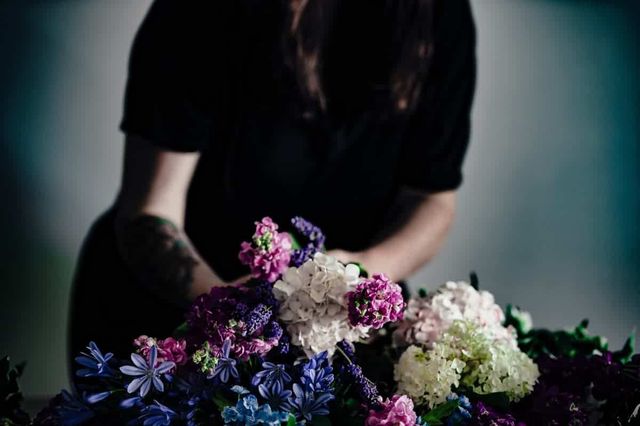 Someone wearing black and holding a bunch of colourful flowers.