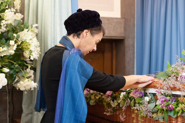 A mourner with their hand on a coffin.
