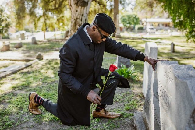 man kneeling at grave in cemetery