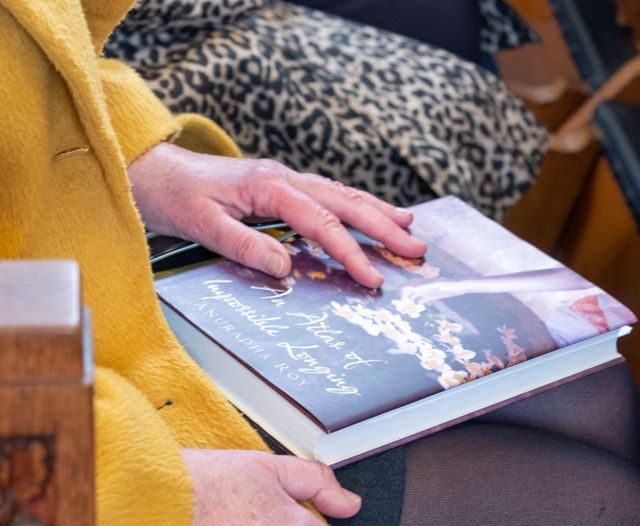 Close up of a woman sat on a church pew with a book on her lap