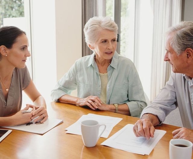 Senior couple with younger woman, planning paperwork and documents in home.