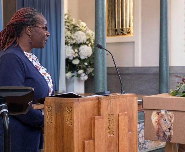Woman speaking at a podium at a funeral with flowers