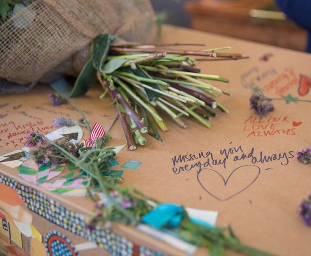 Hand written notes of love and remembrance written on a natural coffin with stickers and flowers