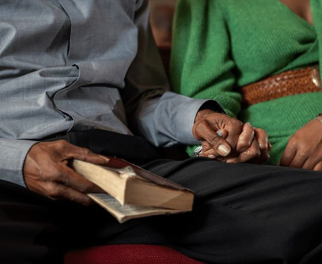 A couple holding hands at church. One of them holds a bible ready for a reading