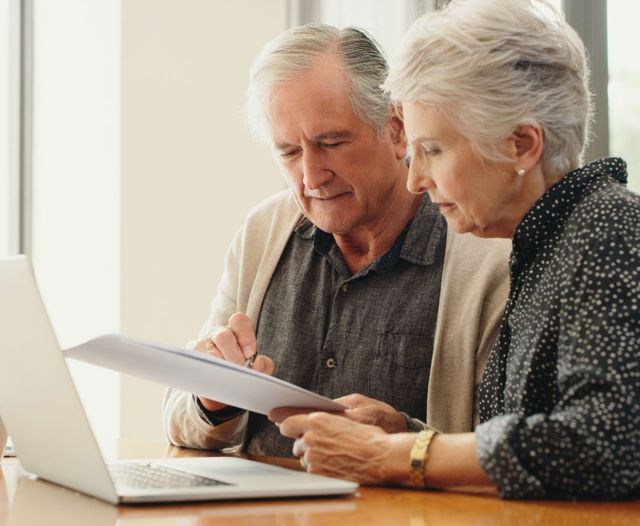 Senior couple with laptop and documents discussing funeral plan expenses at home