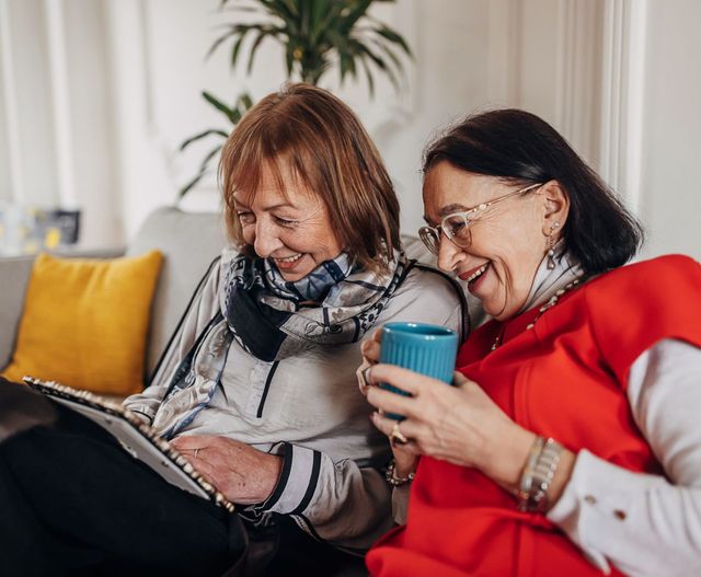 Senior female friends smiling on a sofa in a home setting looking through a photo album