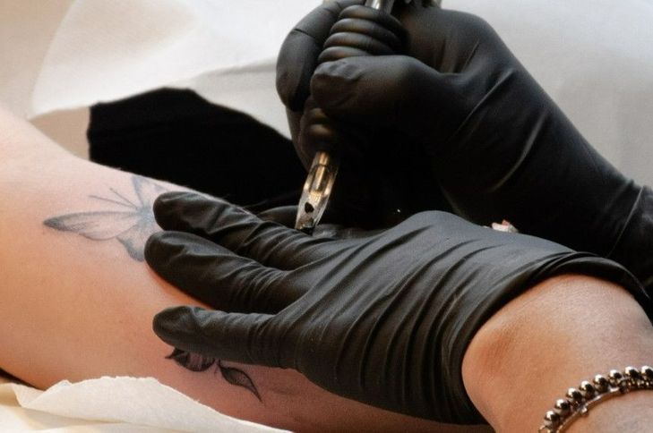 Tattoo artist with black gloves on tattooing a person's arm