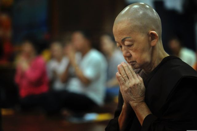 Woman at a Buddhist funeral with her hands in the prayer position.